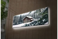 Canvastavla med LED-belysning 30x90 cm - Vinterlandskap med en stuga omgiven av snö och granar