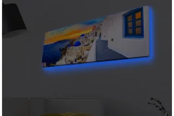 Canvastavla med LED-belysning - Vacker vy över vita hus med blå kupoler mot havet och en färgsprakande solnedgång
