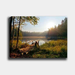 Canvastavla 70x100 cm - Stilla sjö med en träbro omgiven av grönskande träd och morgonsolens strålar