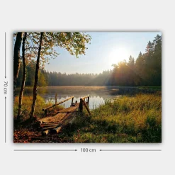 Canvastavla 70x100 cm - Stilla sjö med en träbro omgiven av grönskande träd och morgonsolens strålar