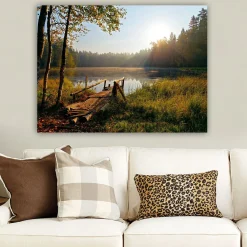Canvastavla 70x100 cm - Stilla sjö med en träbro omgiven av grönskande träd och morgonsolens strålar